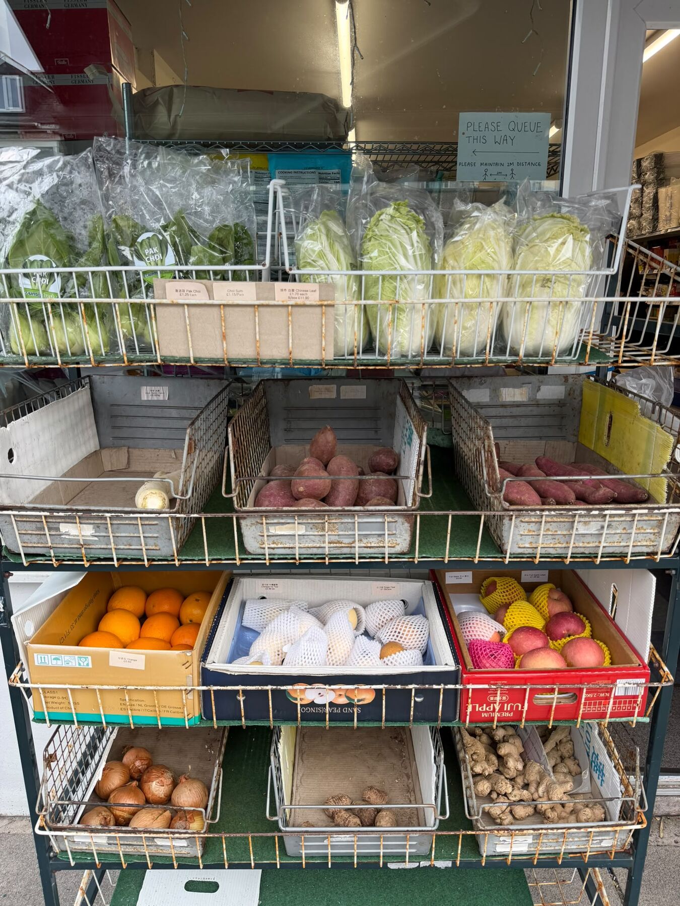 Fresh produce display outside the shop with pak choi, choi sum, Chinese leaf, white and purple sweet potatoes, mooli, oranges, Chinese pears, Fuji apples, mango, brown onions, taro and fresh ginger